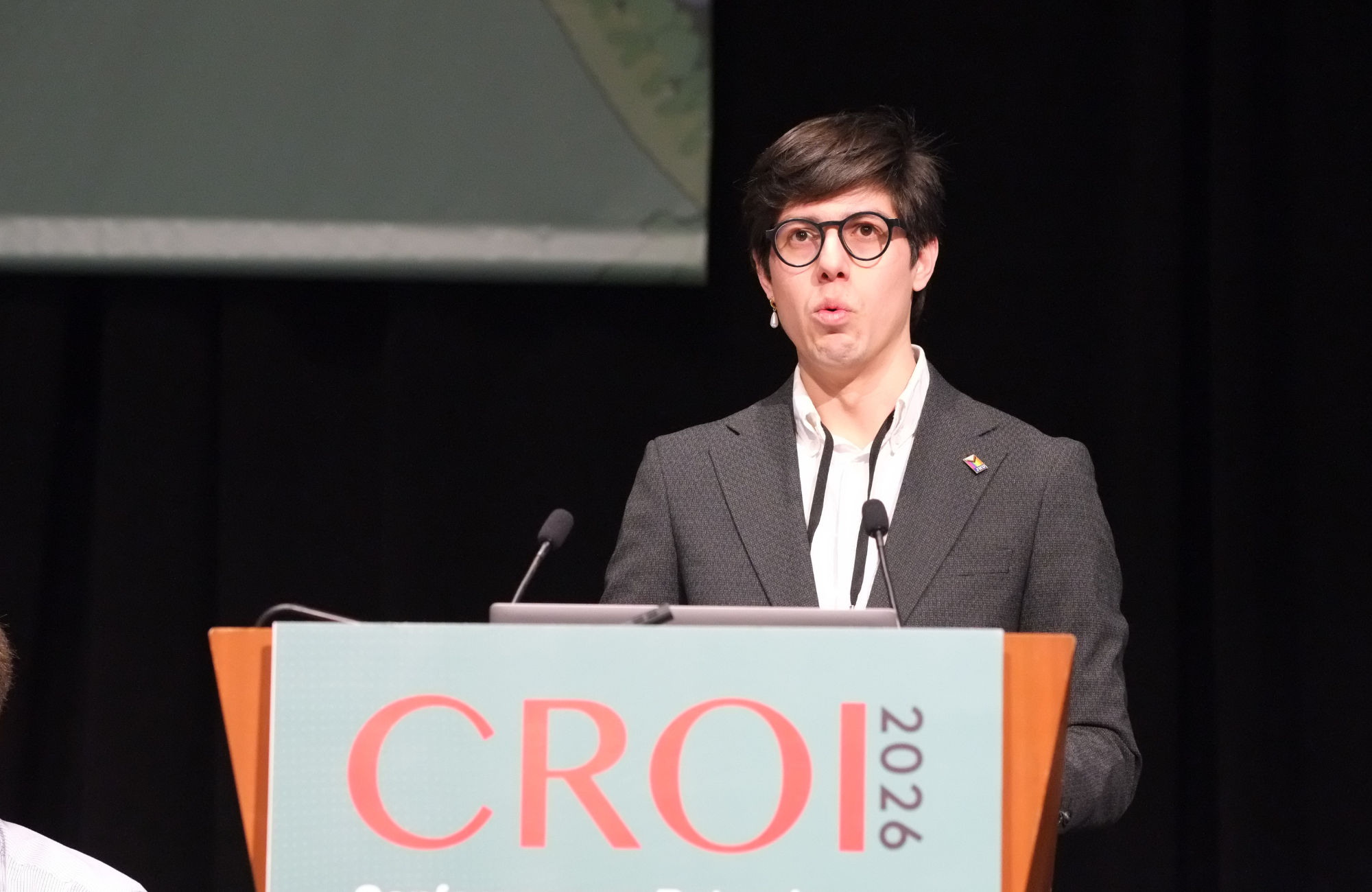 Dr Antonio Bandala-Jacques at CROI 2026. He is standing behind a lectern talking into a microphone.