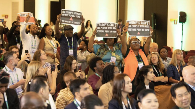 Activists protesting at AIDS 2026. They are holding up placards about 'Trump's cuts'.
