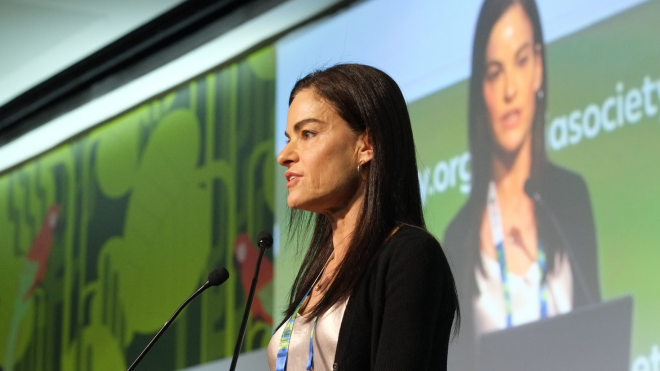 Dr Amy Colson at AIDS 2026. She is talking into a microphone with a screen behind her.