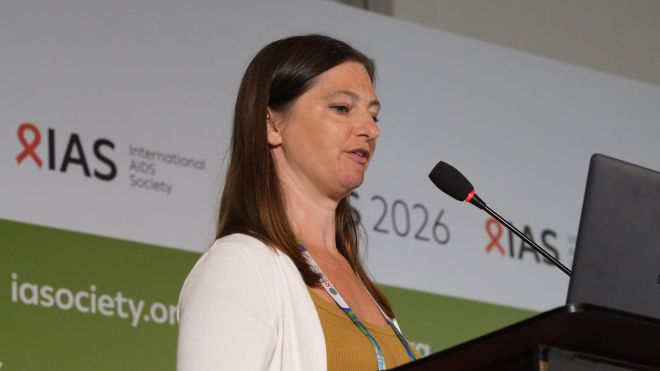 Florence Bascombe at AIDS 2026. She is standing at a lectern, talking into a microphone.