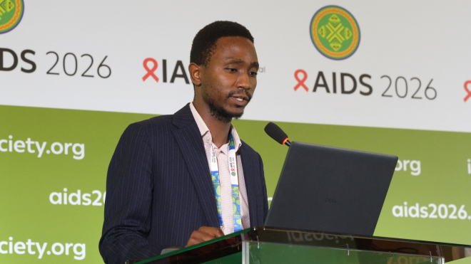 Dr John Fly Phiri at AIDS 2026. He is standing at a lectern, talking into a microphone.