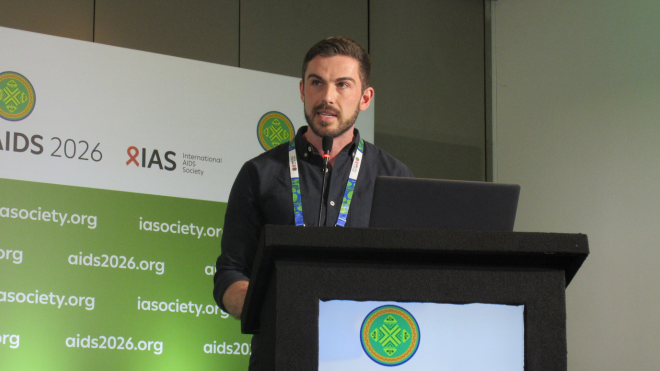 Dr Michael Traeger at AIDS 2026. He is standing at a lectern talking into a microphone.