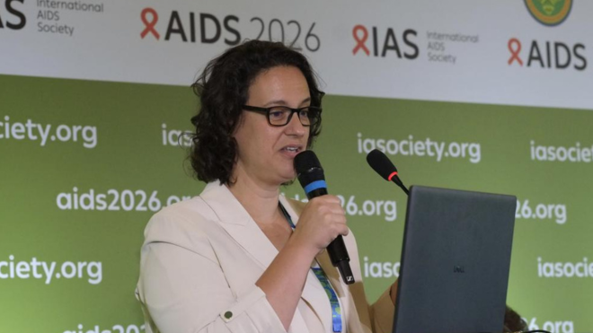 Dr Joana Woods at AIDS 2026. She is talking into a microphone with a laptop screen in front of her.