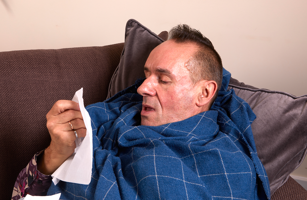 a man who looks unwell, sneezing into a tissue