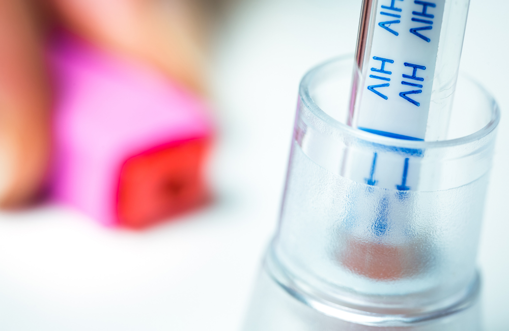 An empty vial marked with the word "HIV" resting in a test tube. The image has a pink and purple filter on it.