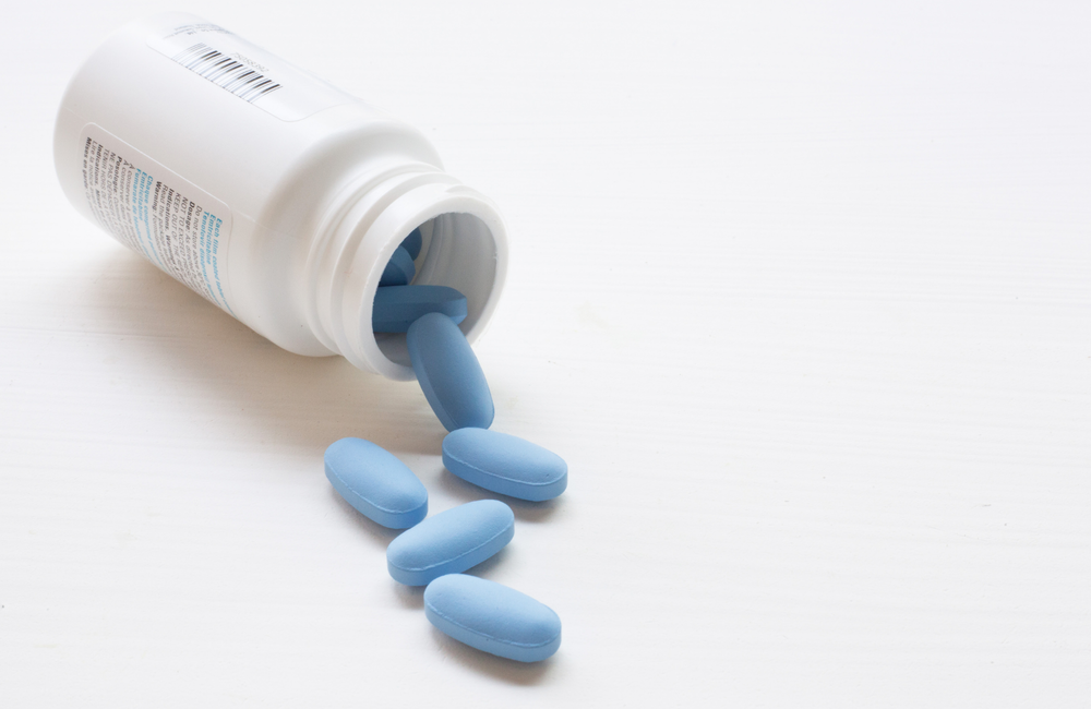 A medication bottle on its side and open, with its contents of oval tablets spilling onto a white surface. The image has a pink and purple filter on it.  