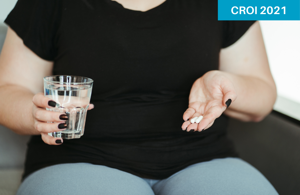 A women sitting on a sofa holding pills and a glass of water. Flotsam/Shutterstock.com