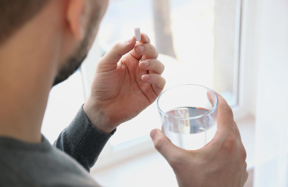 A person taking a white pill holding a glass of water.