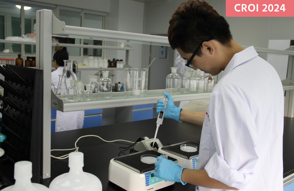 A person in a white coat in a laboratory holding a pipette.