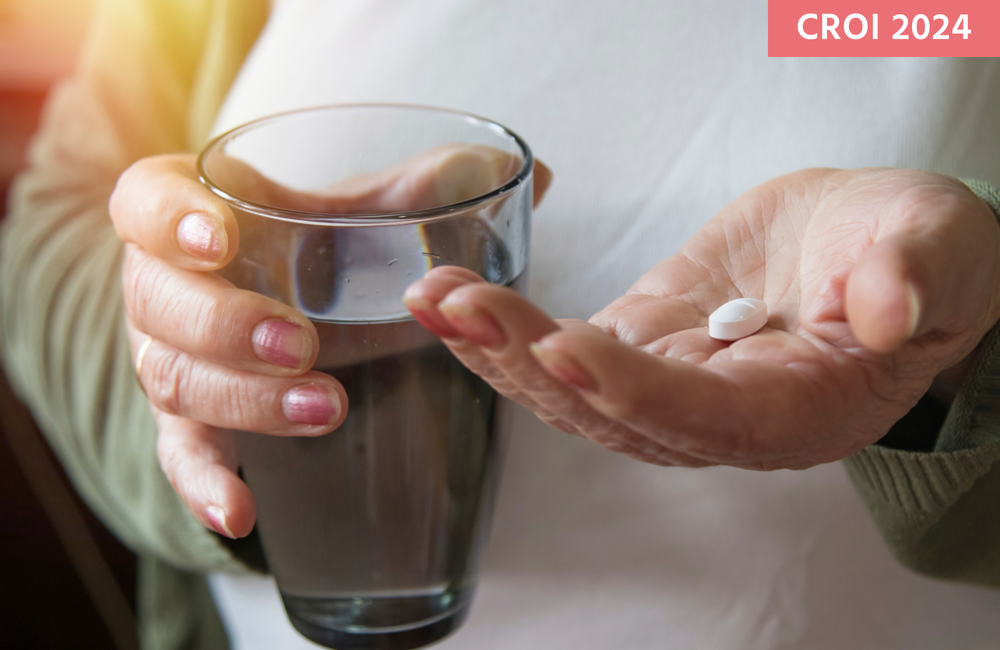 A person holding a white pill and a glass of water.