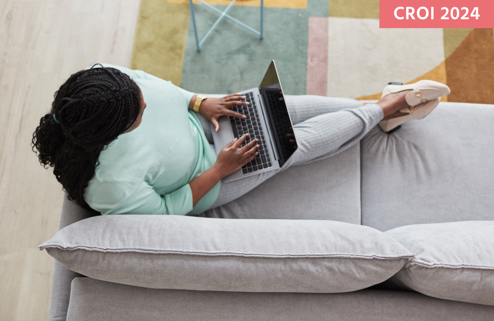 A Black woman sitting on a sofa using a laptop.