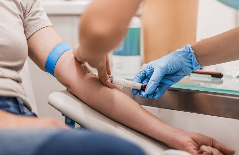 A person having a blood test. They are sitting in a chair while a nurse collects blood in a vial.