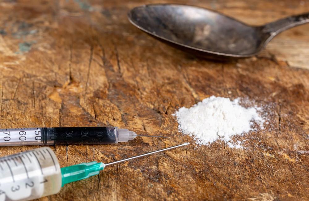 Two syringes, powder and spoon on old wooden background.