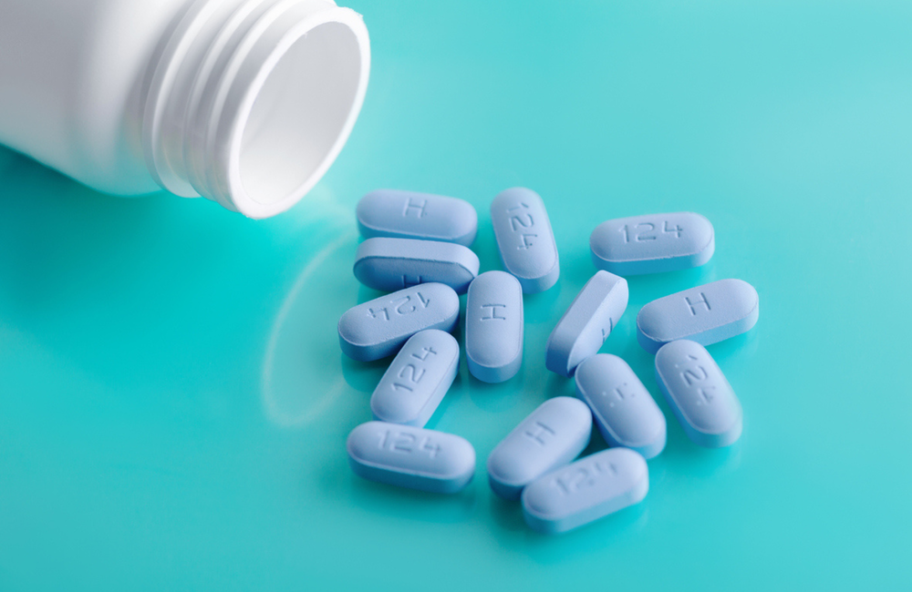 A white bottle of pills is on its side with blue PrEP pills spilling out, on a turquoise background