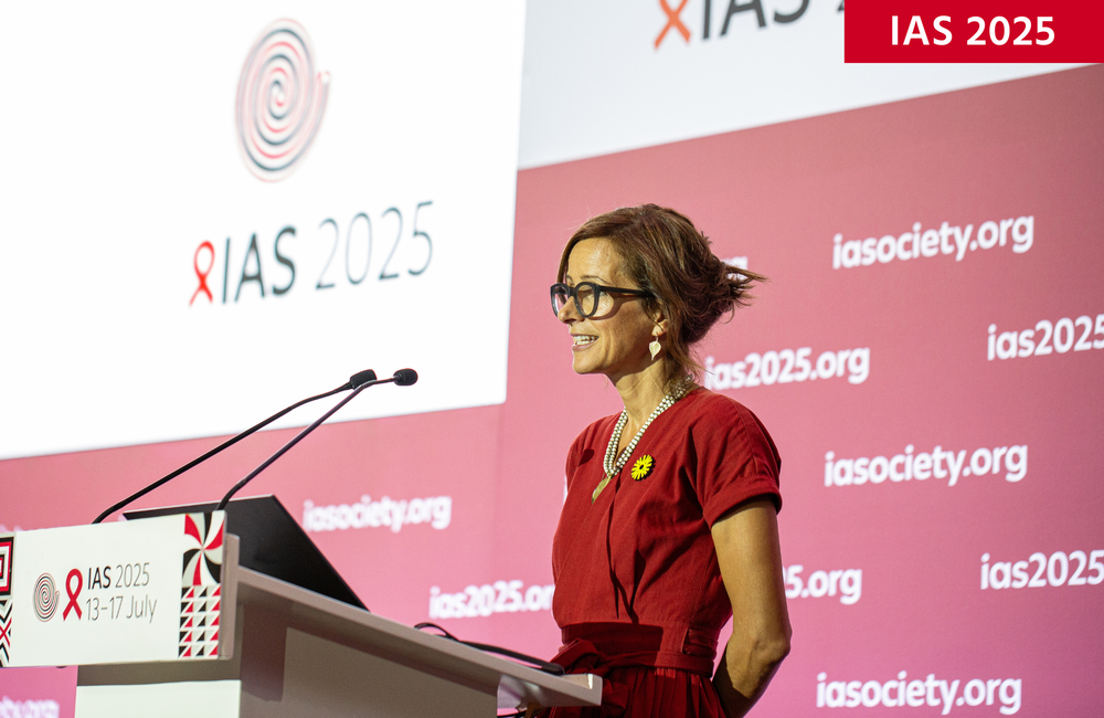 Dr Fiona Cresswell at IAS 2025. ©Jacques Nkinzingabo/IAS. CC BY-SA 4.0. Dr Fiona Cresswell at IAS 2025. She is wearing a red top and has brown hair. She is talking into a microphone behind a podium.