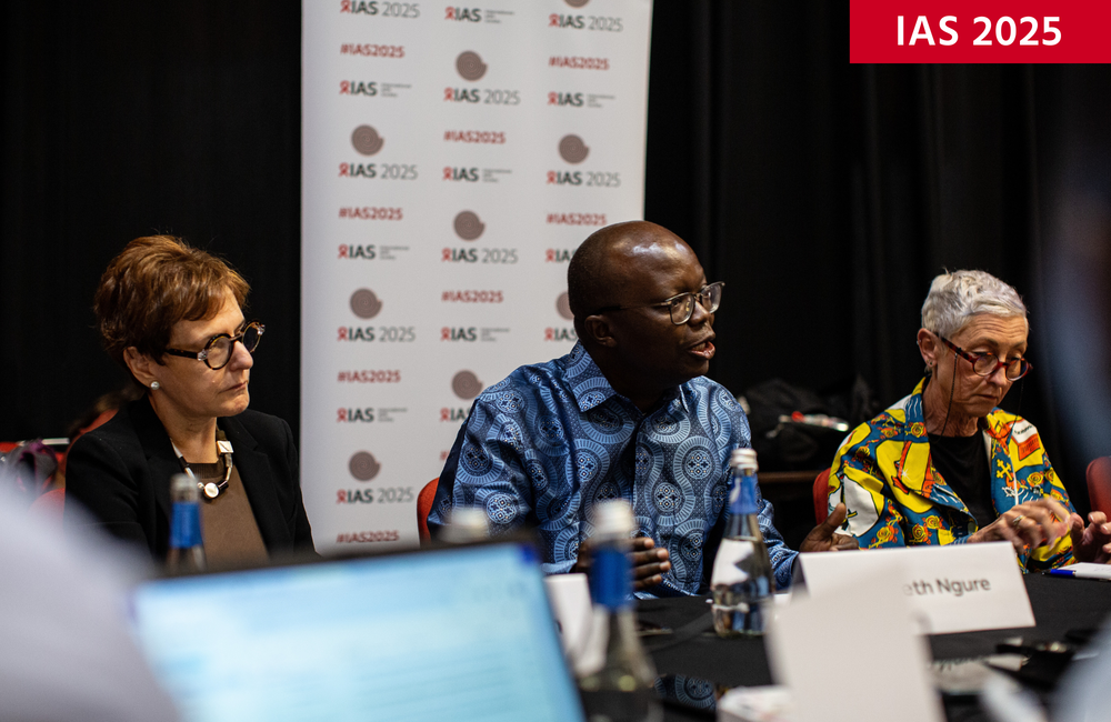 Kenneth Ngure (centre), IAS President-elect, at IAS 2025. ©Jacques Nkinzingabo/IAS. CC BY-SA 4.0. Kenneth Ngure, IAS President-elect, at IAS 2025. He is sitting between two people, talking into a microphone.