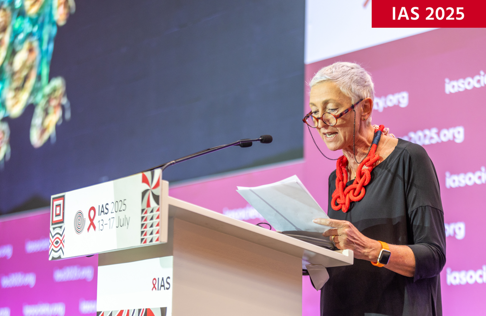 Professor Linda-Gail Bekker at IAS 2025. ©Jean Bizimana/IAS. CC BY-SA 4.0. Professor Linda-Gail Bekker at IAS 2025. She has short grey hair and is wearing a black top. She's standing behind a podium.