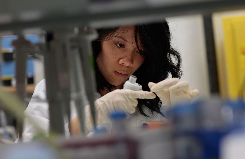 Close-up of a researcher working in a lab. She is wearing white surgical gloves and a white lab coat.