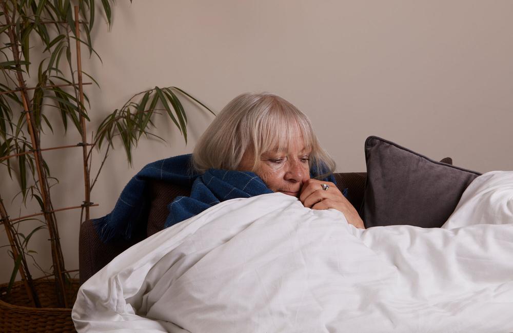 A woman site on the sofa with a blanket over her and around her shoulders.