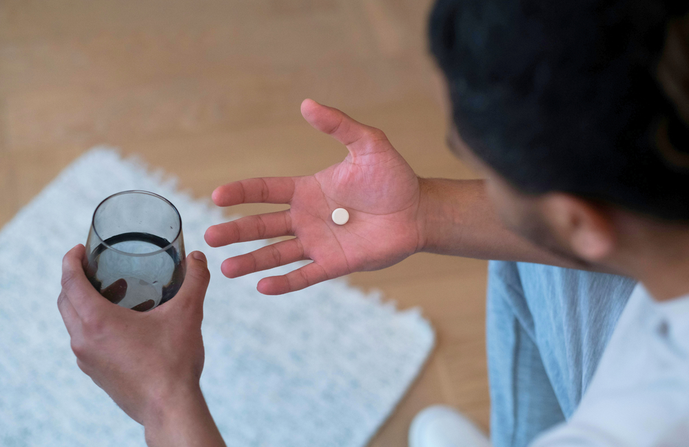 A person is holding a white pill and a glass of water.