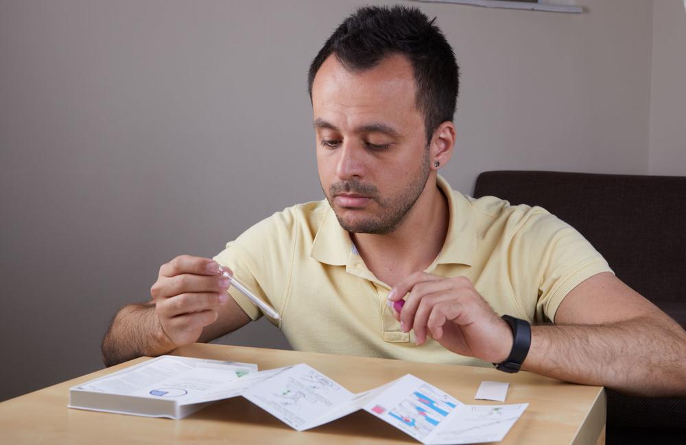 A man reads a leaflet while holding a self-sampling pipette.