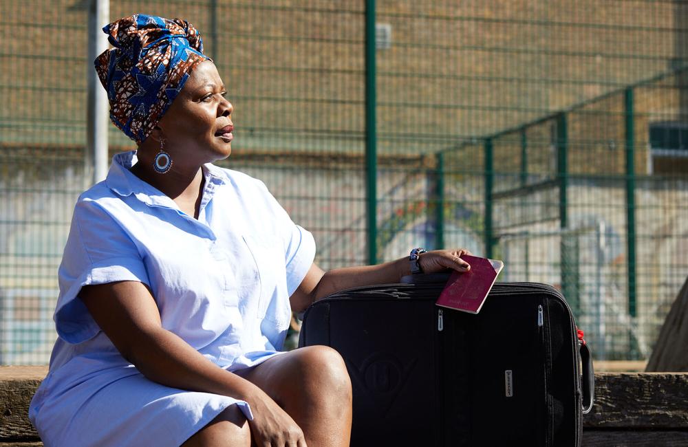 A woman sits outside with a suitcase, holding a passport.