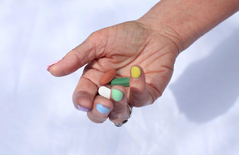 A hand holding green, white and brown pills.