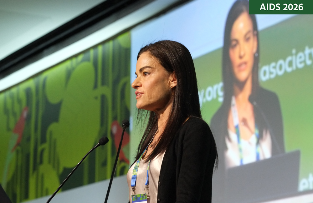 Dr Amy Colson at AIDS 2026. She is talking into a microphone with a screen behind her.