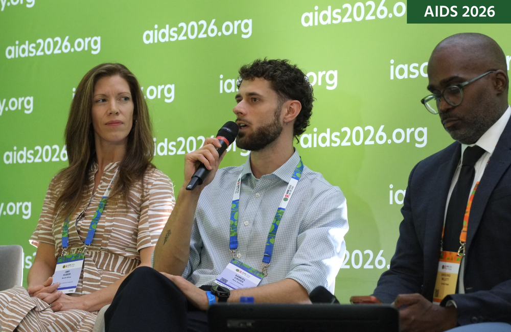 Dr Samuel Cross sits between two other people at a media conference. He is talking into a microphone.