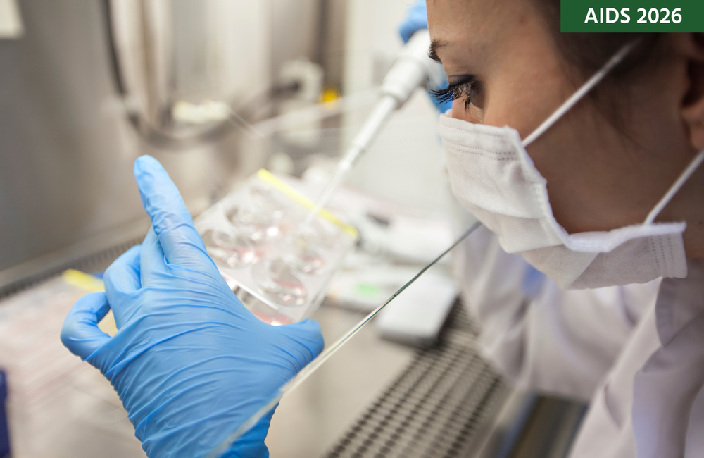 Close-up of a researcher in a lab wearing a mask and blue gloves, holding a large pipette and a tray of samples.