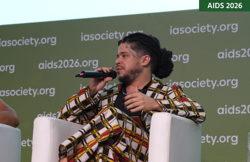 Thiago Jerohan Albuquerque da Cruz at AIDS 2026. He is sitting down and talking into a microphone at a press conference.