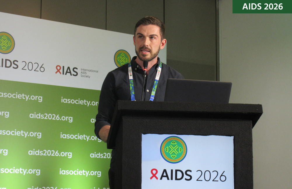 Dr Michael Traeger at AIDS 2026. He is standing at a lectern talking into a microphone.